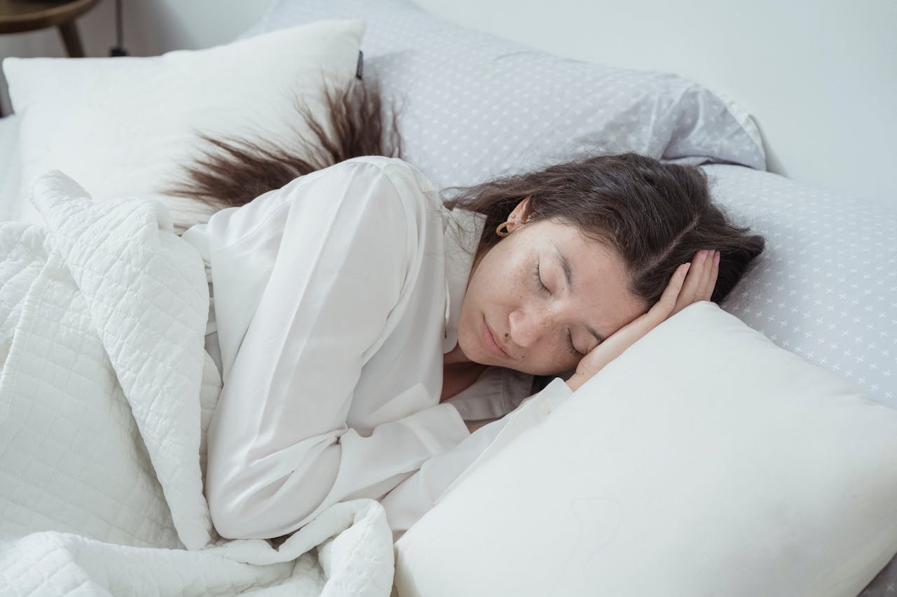 Home A serene woman rests comfortably in bed with soft pillows and blankets, embracing relaxation.